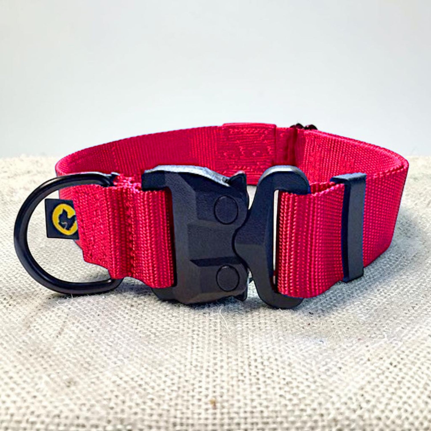 Thick red dog collar with a strong black buckle on a burlap fabric surface